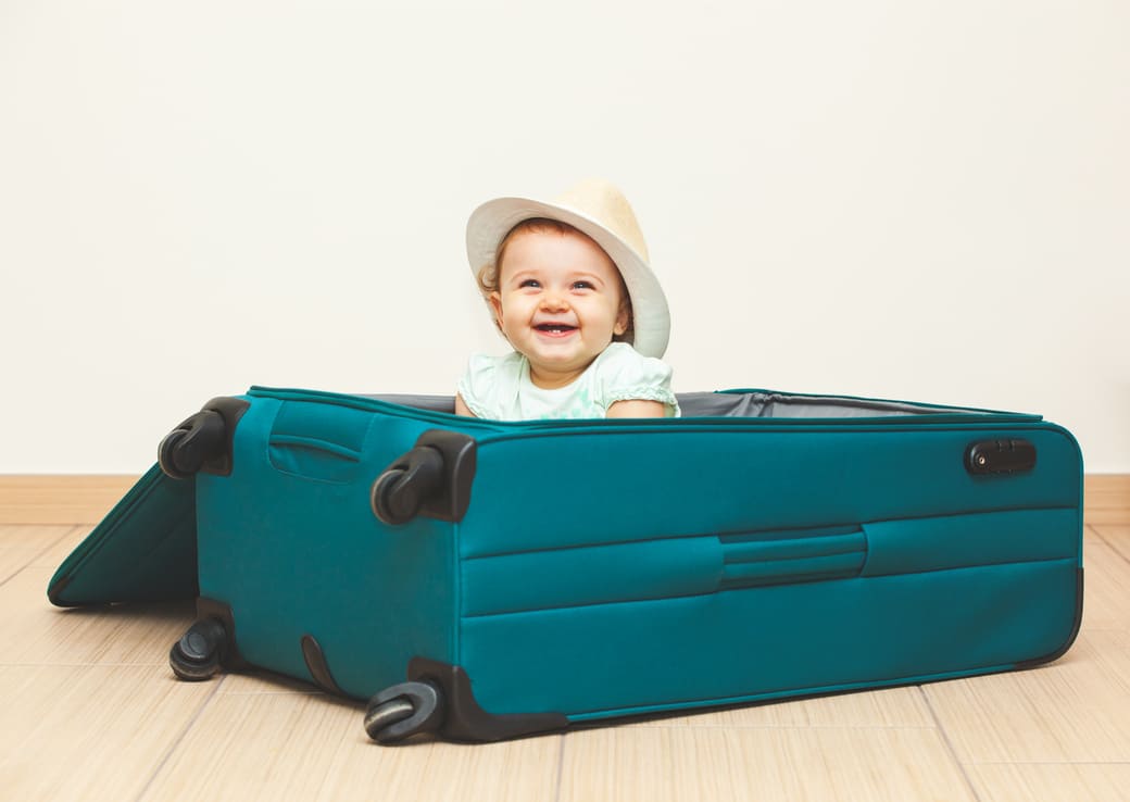 Petite fille portant un chapeau assise dans une valise