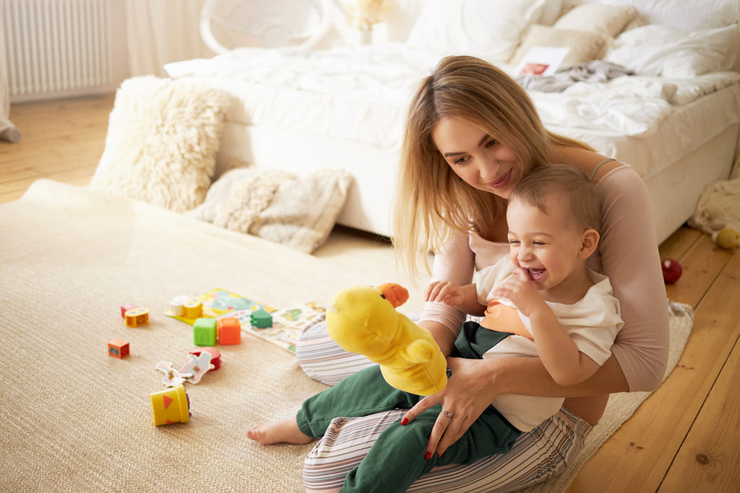 belle jeune baby-sitter jouant avec petit garçon à l'intérieur, tenant un canard en peluche.