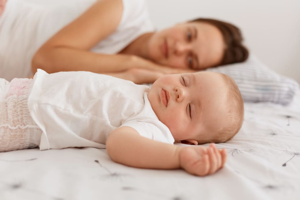 femme aux cheveux noirs portant un t-shirt blanc allongé sur le lit avec son bébé